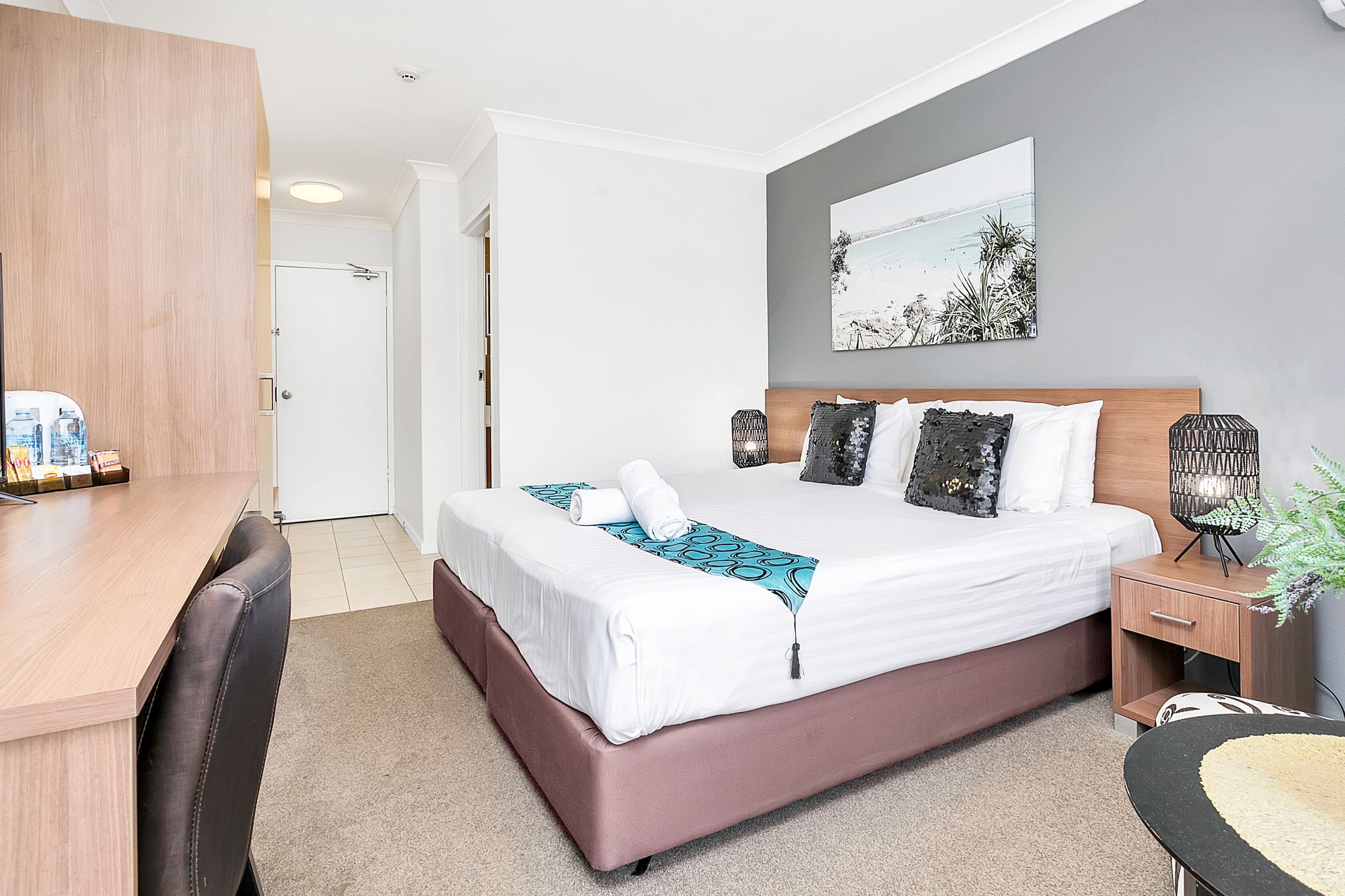 Ein modernes Hotelzimmer mit einem großen Bett, einem Holztisch, einem Nachttisch und einem an der Wand hängenden Kunstwerk.