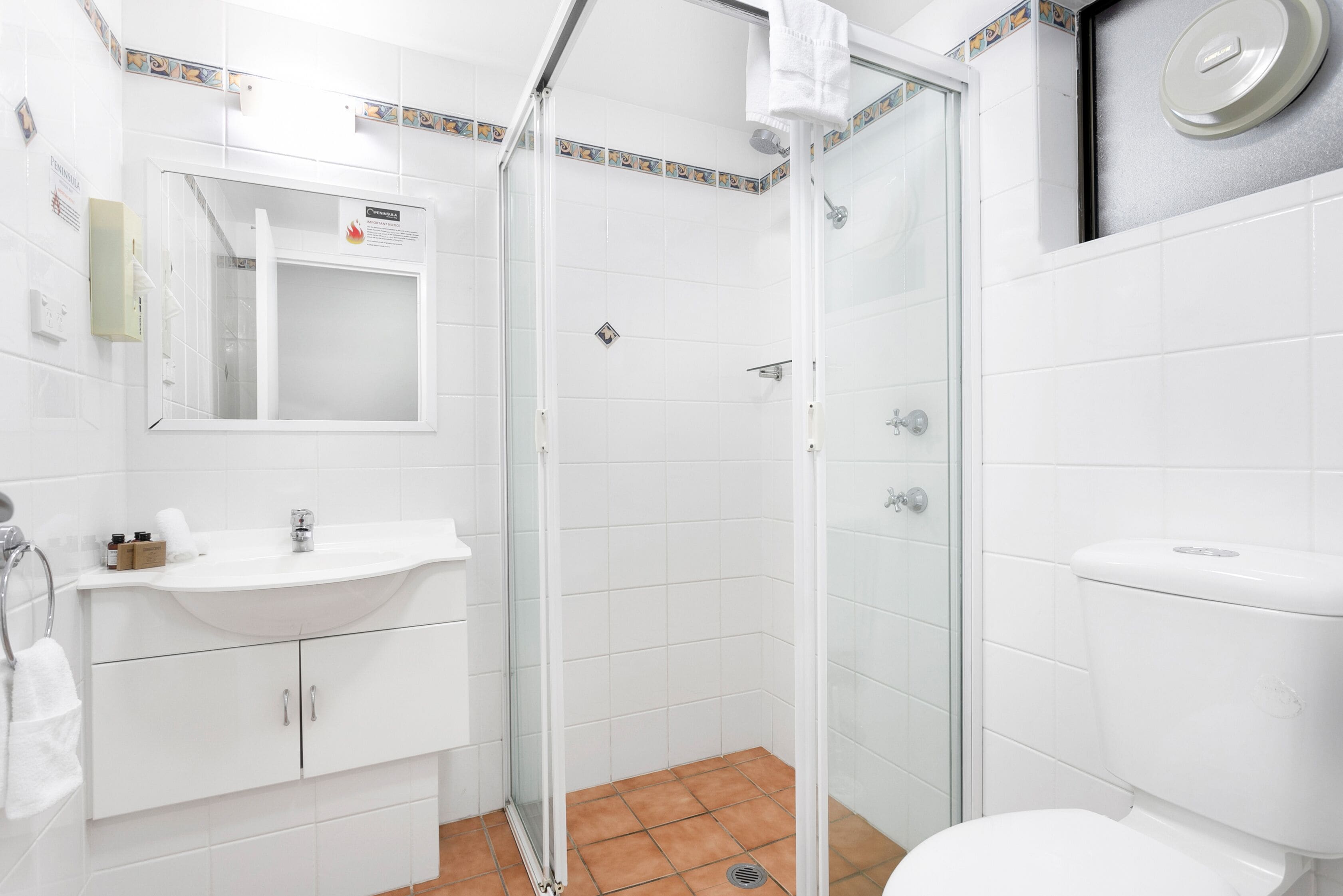 A bathroom with a white sink, mirror, and toilet, a glass-enclosed shower, and a tiled floor.
