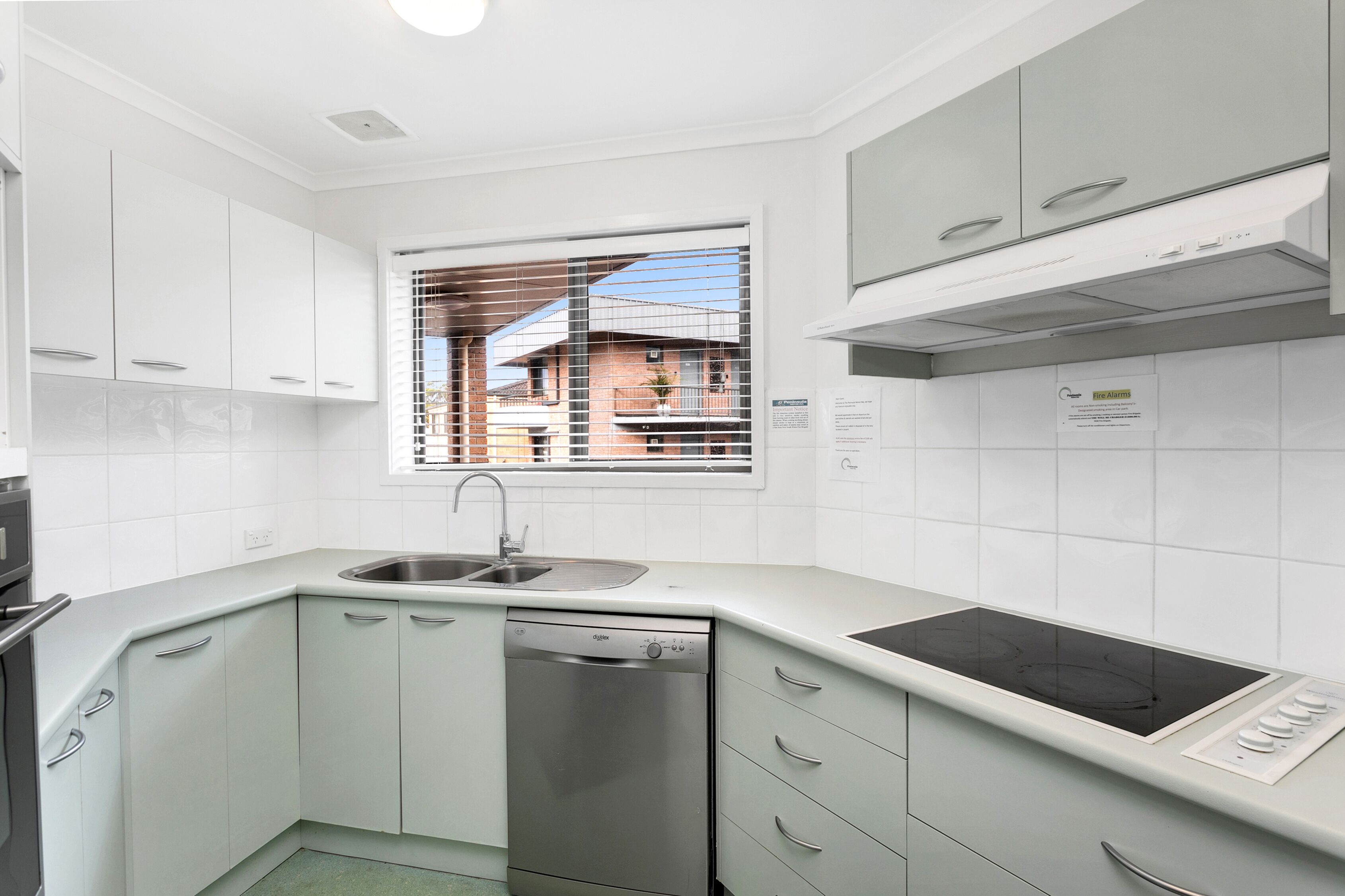 A modern kitchen with white cabinets, a dishwasher, a sink, and a window with blinds.
