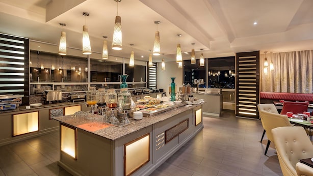 A modern kitchen with a central island, pendant lighting, and a dining area with chairs and tables.