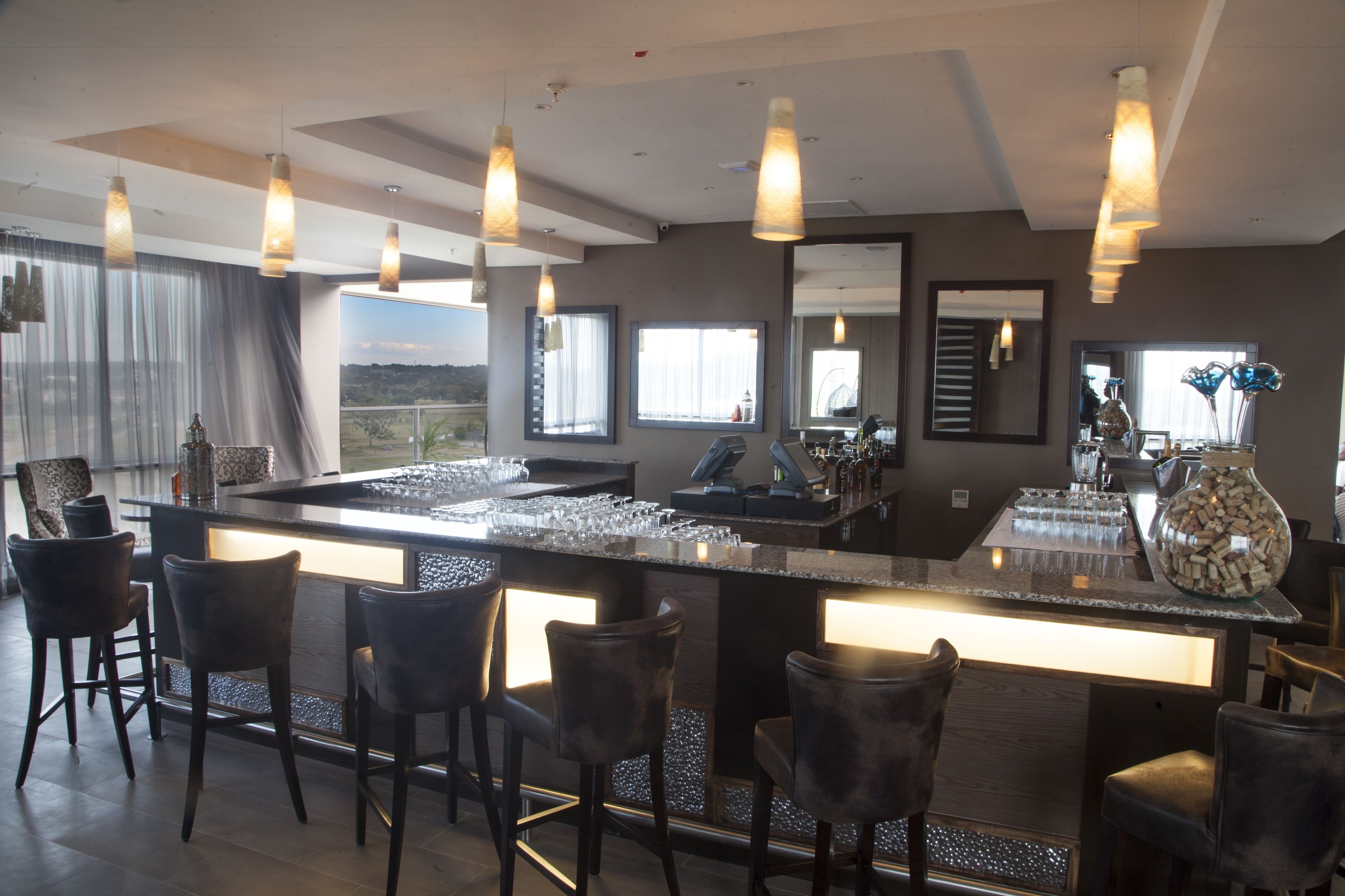 Una zona de bar moderna con una barra alargada, varios taburetes y luces colgantes.