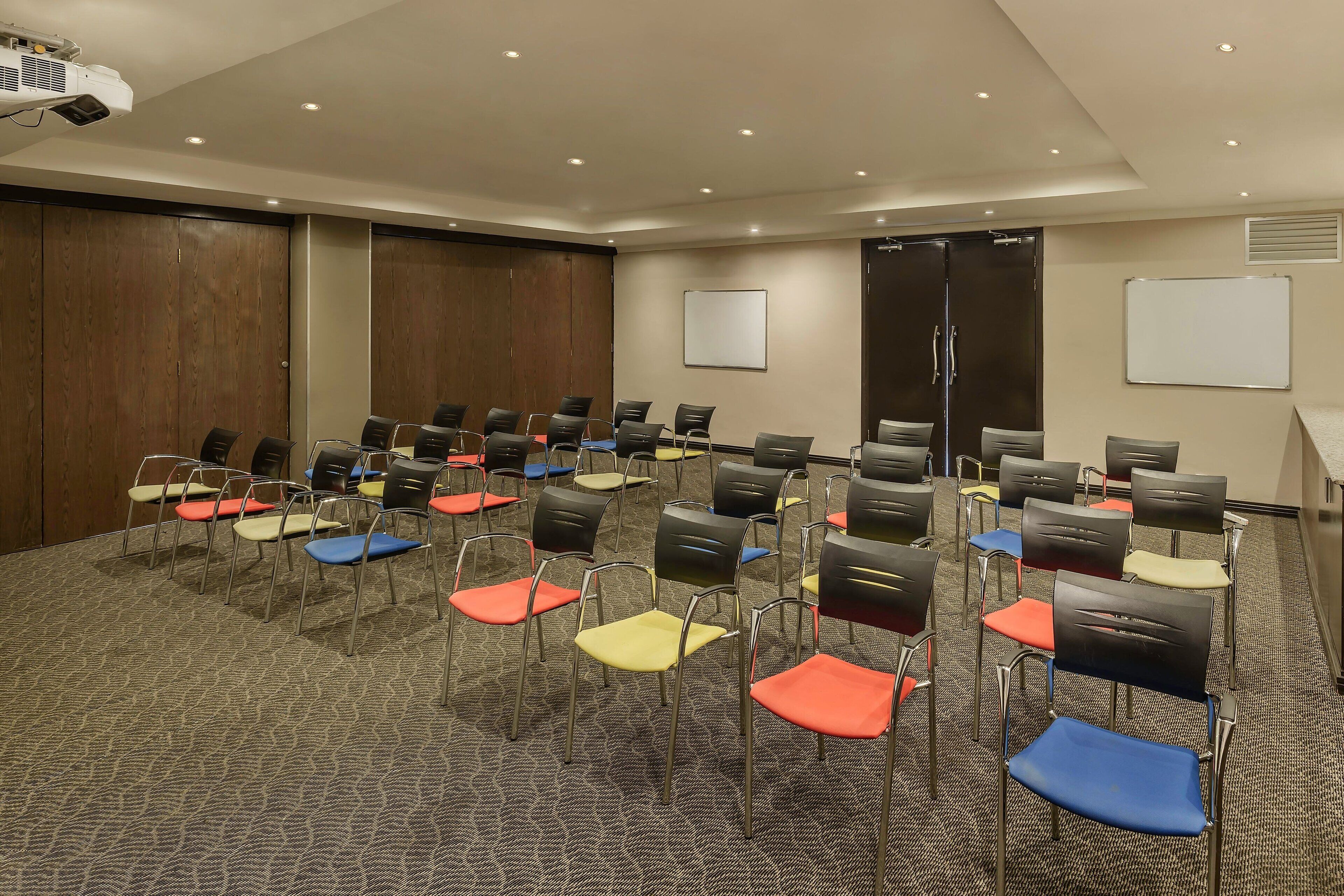 Une salle de conférence avec des rangées de chaises, un projecteur et un tableau blanc.
