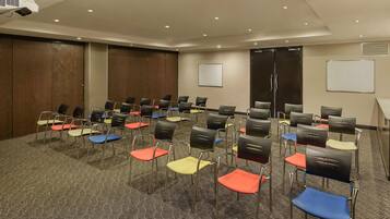 Une salle de conférence avec des rangées de chaises, un projecteur et un tableau blanc.