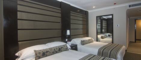 Una habitación de hotel con dos camas, una mesita de noche, una lámpara y un espejo.