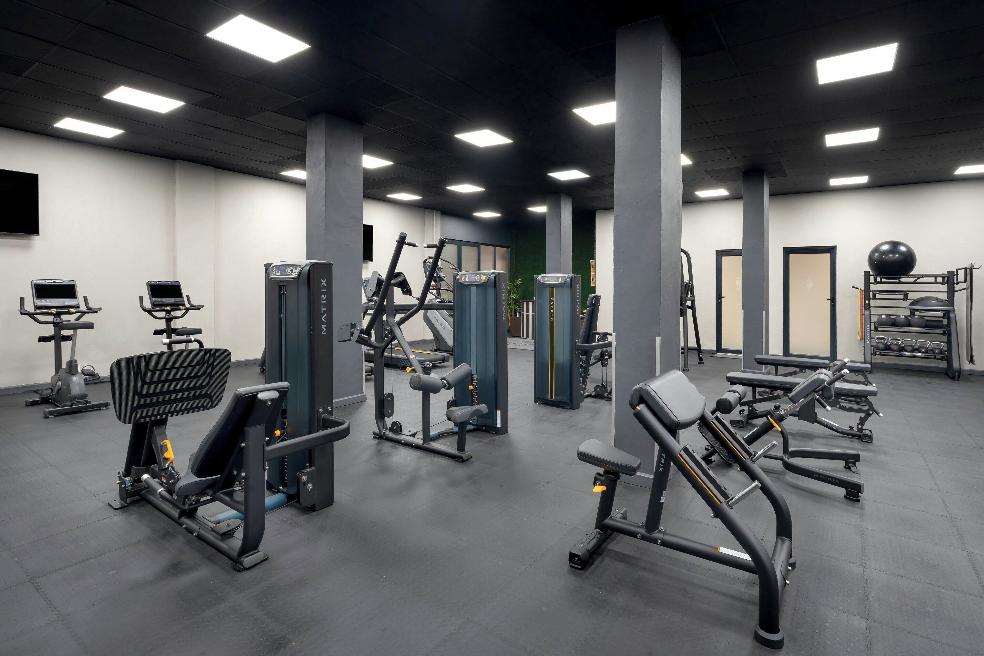 Ein Fitnessstudio mit verschiedenen Trainingsgeräten, darunter Laufbänder, Kraftgeräte und eine Langhantelbank.