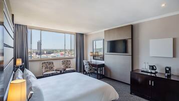Habitación de hotel con una cama grande, escritorio, silla, televisión y minibar.
