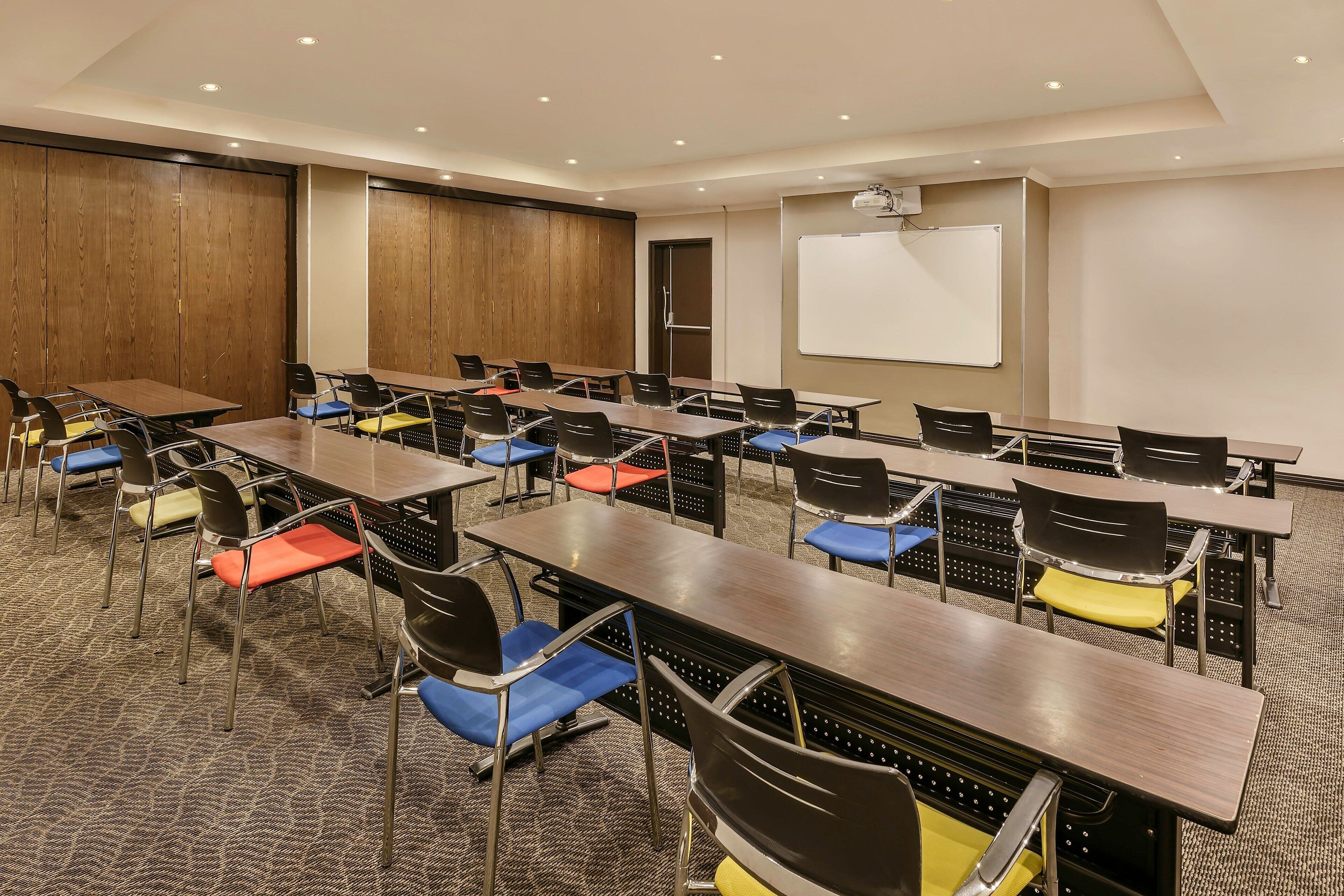A conference room with multiple tables and chairs, a whiteboard, and a projector.