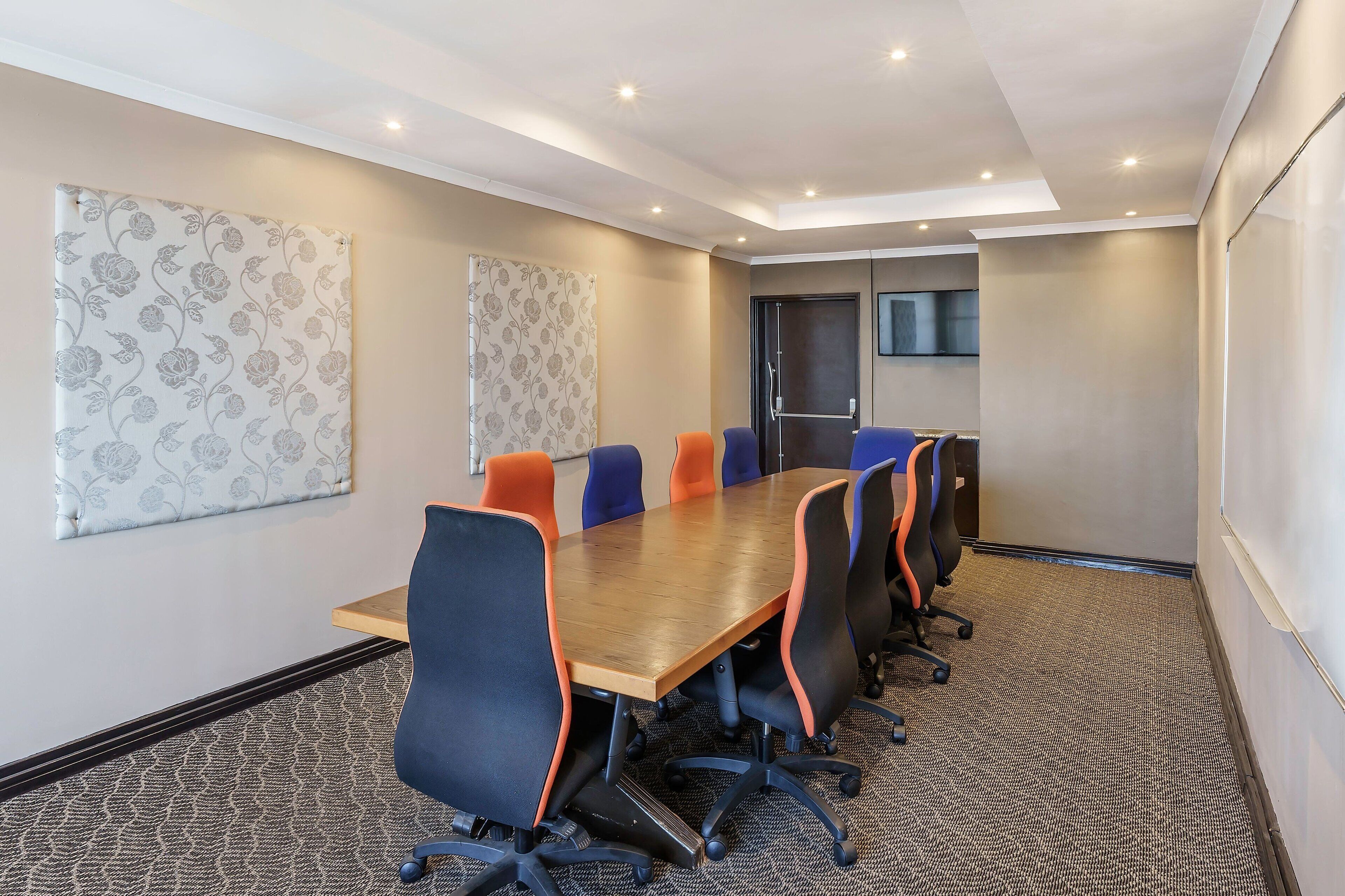 A conference room with a long table, six chairs, and a carpeted floor.