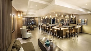 A modern bar area with a high bar counter, multiple stools, and pendant lighting.