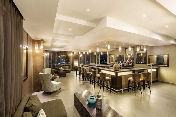 A modern bar area with a high bar counter, multiple stools, and pendant lighting.