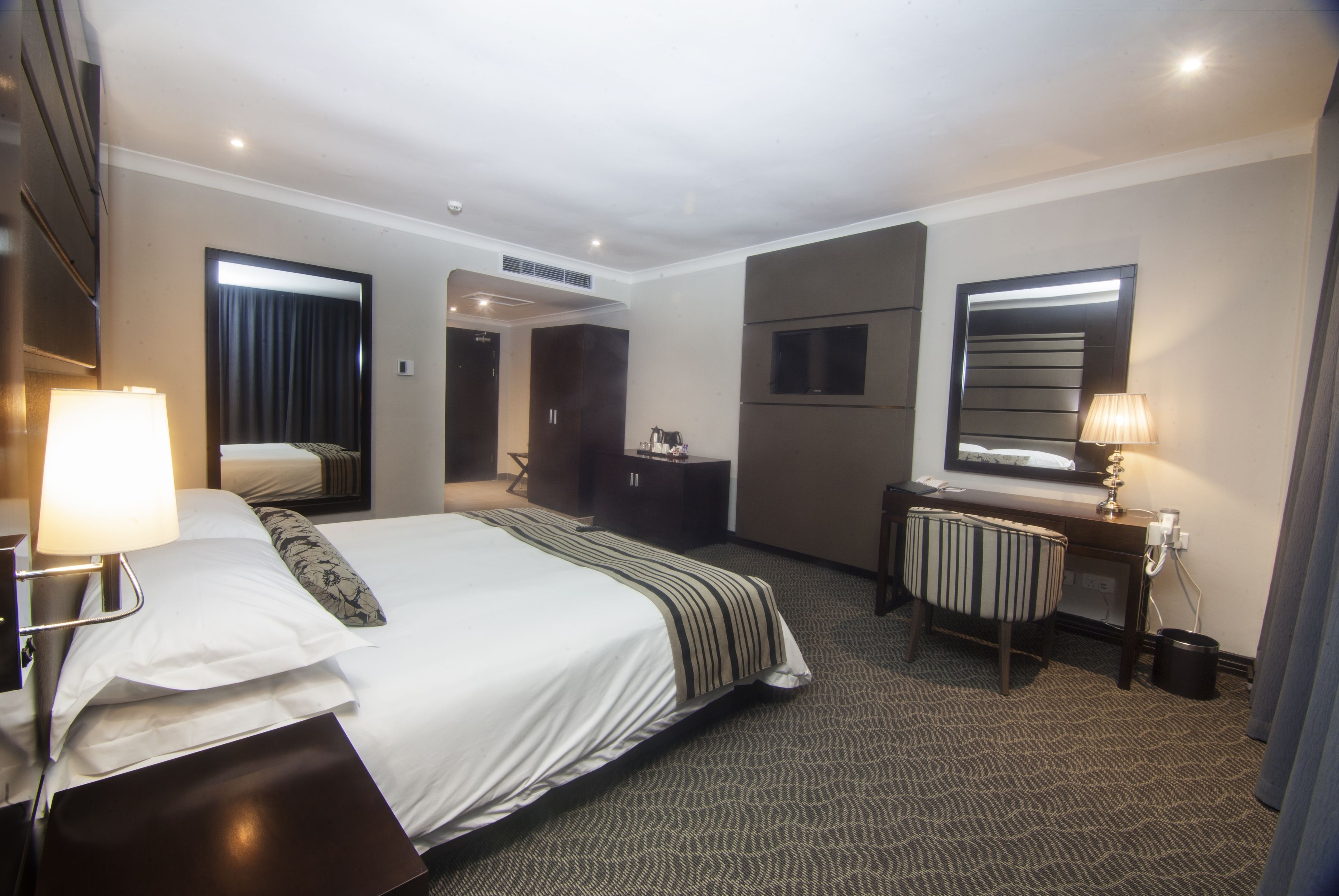 A hotel room with a large bed, a desk with a lamp, a chair, and a television.