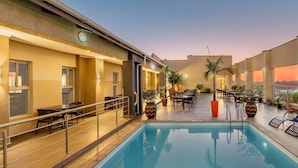 A rooftop pool area with a pool, seating, and potted plants.