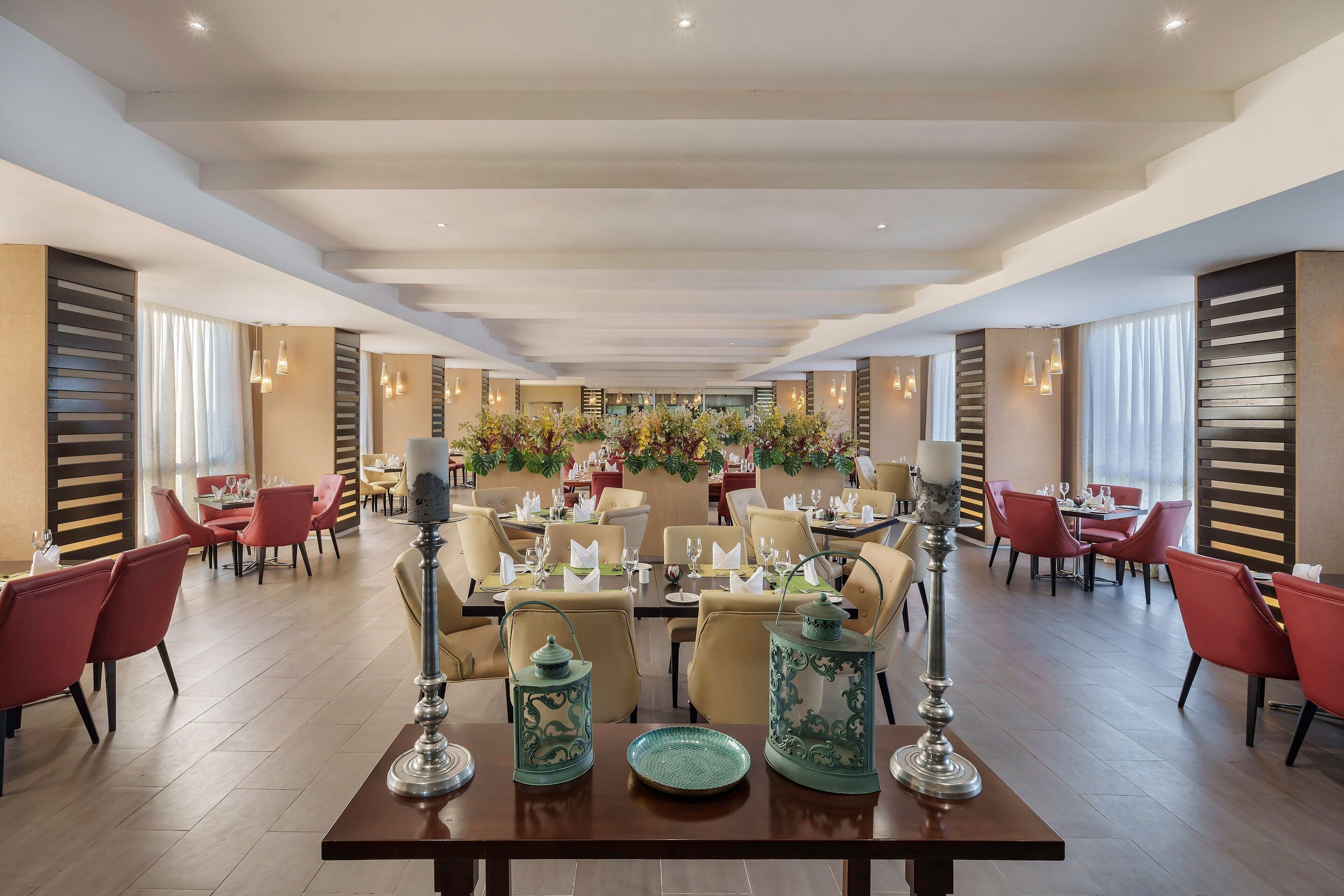 A spacious dining area with multiple tables, red and beige chairs, and decorative lanterns.