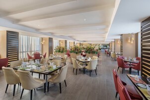 Un comedor amplio con varias mesas y sillas, con un diseño interior moderno que utiliza tonos neutros y plantas decorativas.