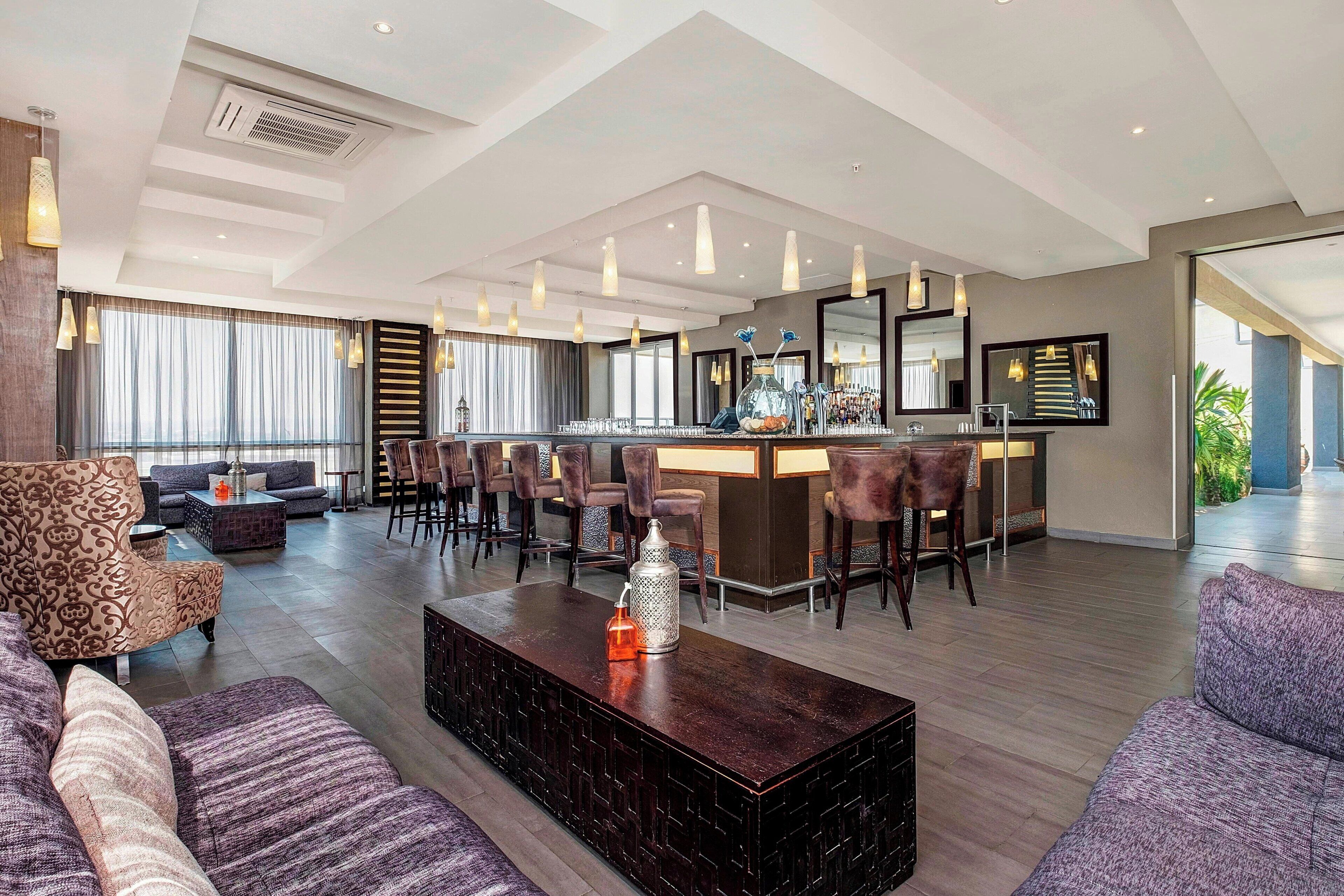 A modern hotel lobby with a bar area, seating arrangements, and a large mirror.
