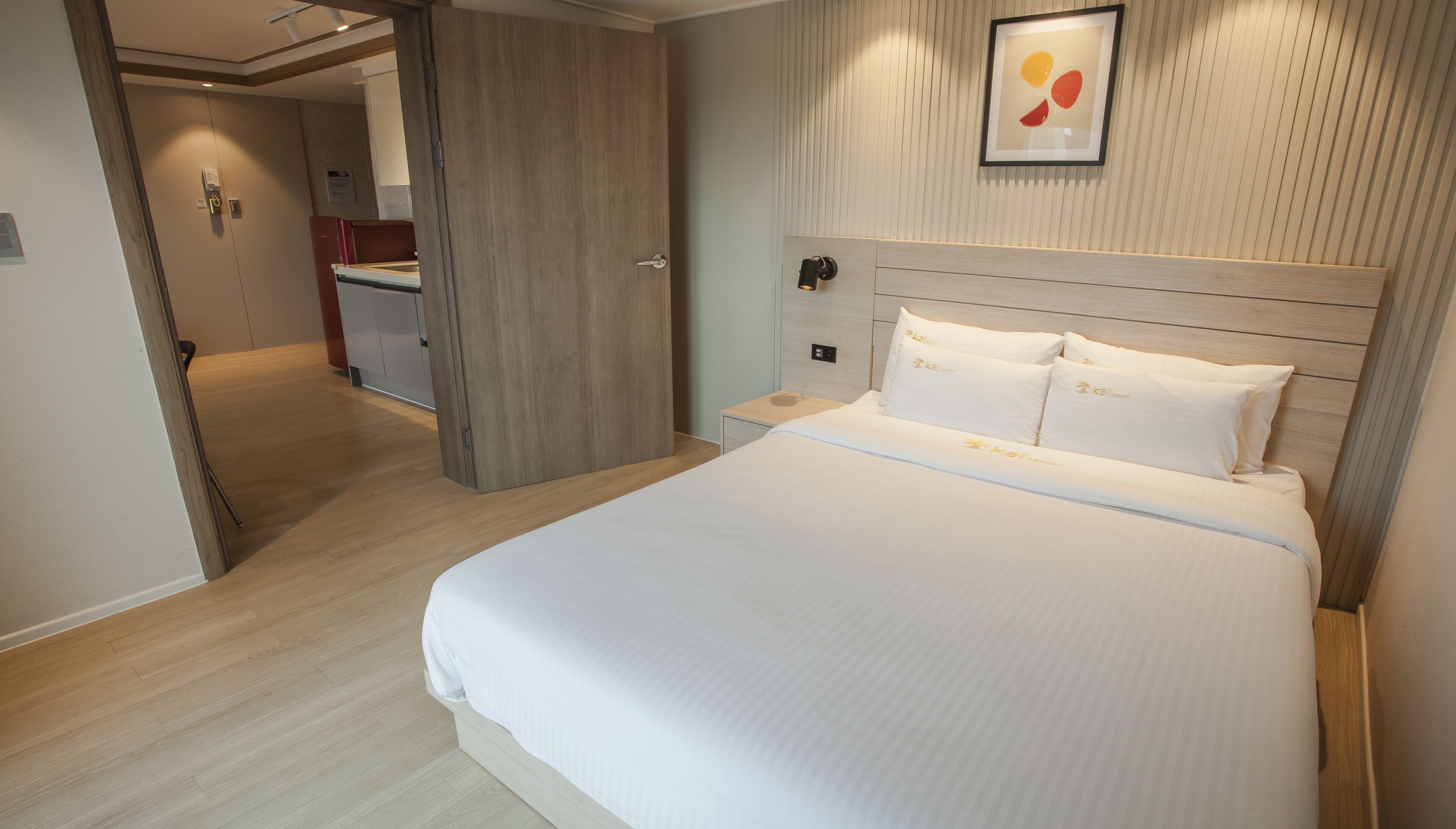 A hotel room with a large bed, a wooden headboard, a nightstand, and a wall-mounted light fixture.