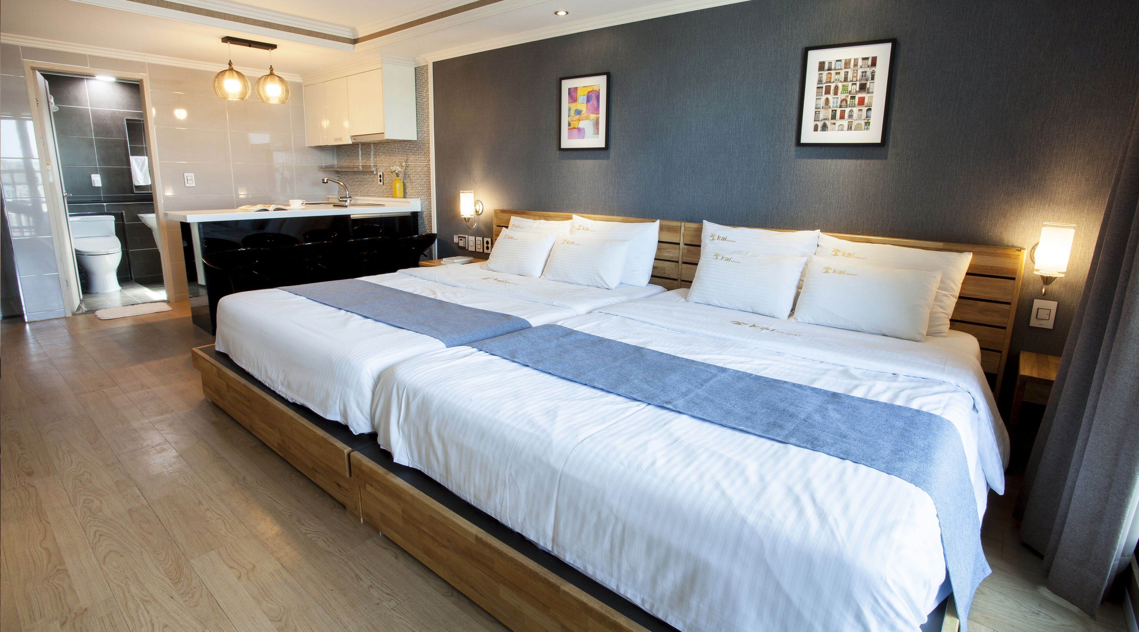 Une chambre d’hôtel avec un grand lit, une tête de lit en bois, une table de chevet, un bureau avec une chaise, une salle de bain avec des toilettes et un lavabo.