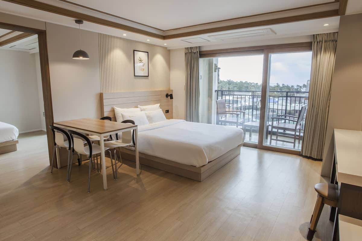 A hotel room with a bed, a desk, chairs, a TV, and a balcony with a view.