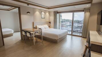 Habitación de hotel con cama, escritorio, sillas, televisor y balcón con vistas.