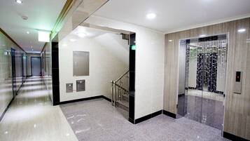 A modern lobby with a marble floor, a staircase, and a glass elevator.