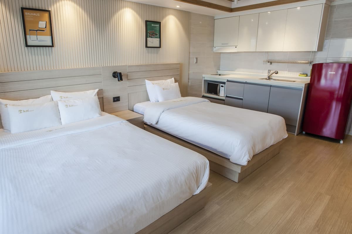 A hotel room with two beds, a kitchenette, and a red refrigerator.