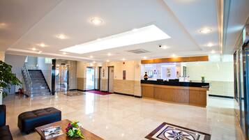 A hotel lobby with a reception desk, a staircase, and a seating area with a coffee table.