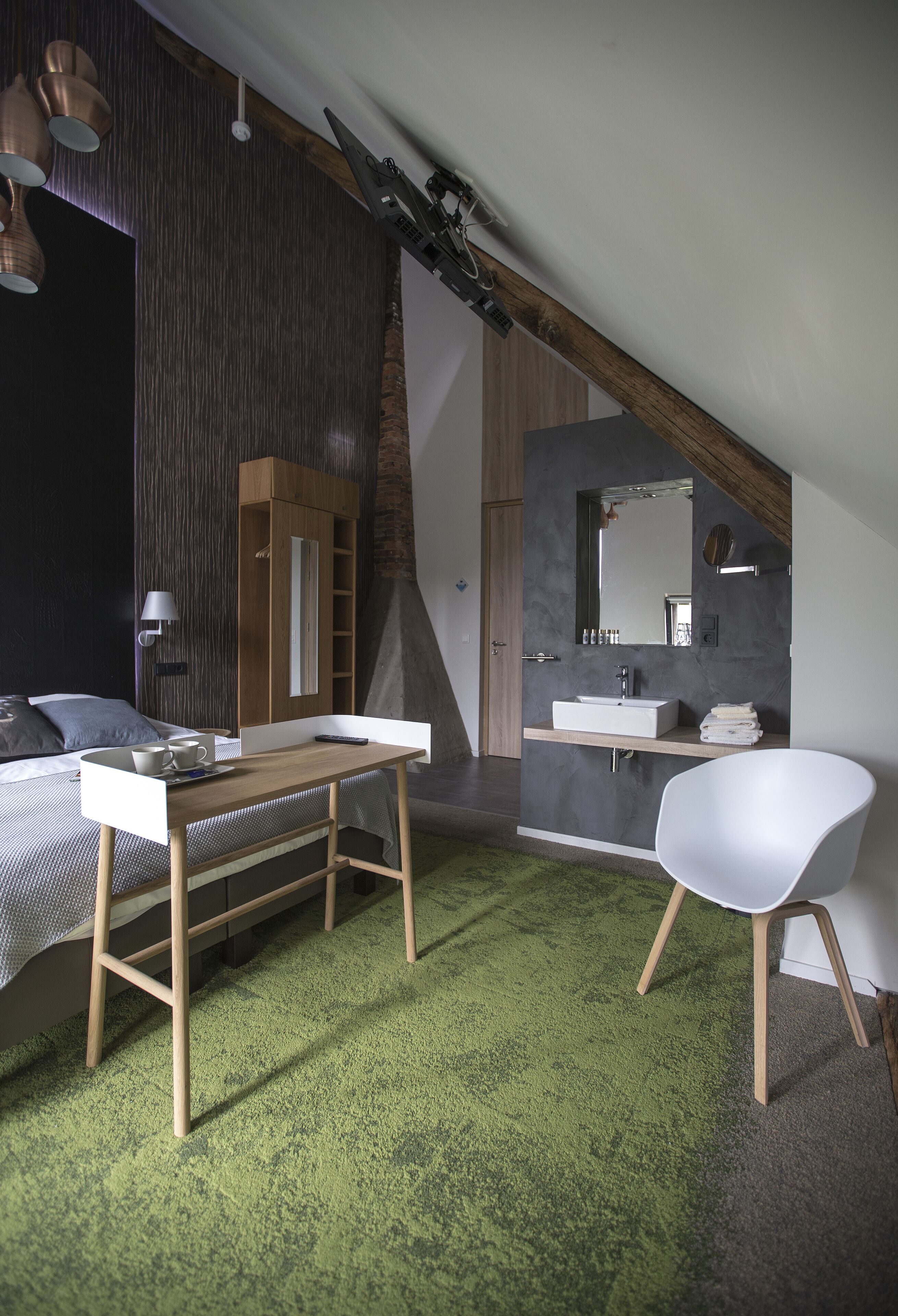 Quarto moderno com cama, escrivaninha, cadeira, banheiro com pia e espelho, e tapete verde.