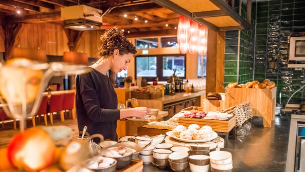 A person serving food in a restaurant with a variety of dishes and drinks on display. - Erfgoed Bossem (Lattrop)