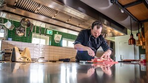 A chef preparing food in a modern kitchen with stainless steel appliances and green tiled walls. - Erfgoed Bossem (Lattrop)