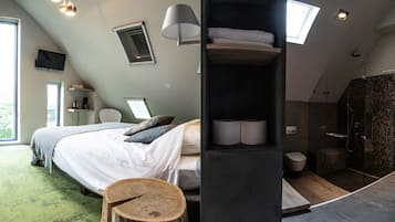 Ein modernes Schlafzimmer mit einem großen Bett, einem hölzernen Hocker, einer eingebauten Ablage mit Handtüchern, einem Fernseher und einem Oberlicht.
