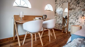 A modern bedroom with a wooden desk, two white chairs, a bed with a blue headboard, and a large mirror. - Erfgoed Bossem (Lattrop)
