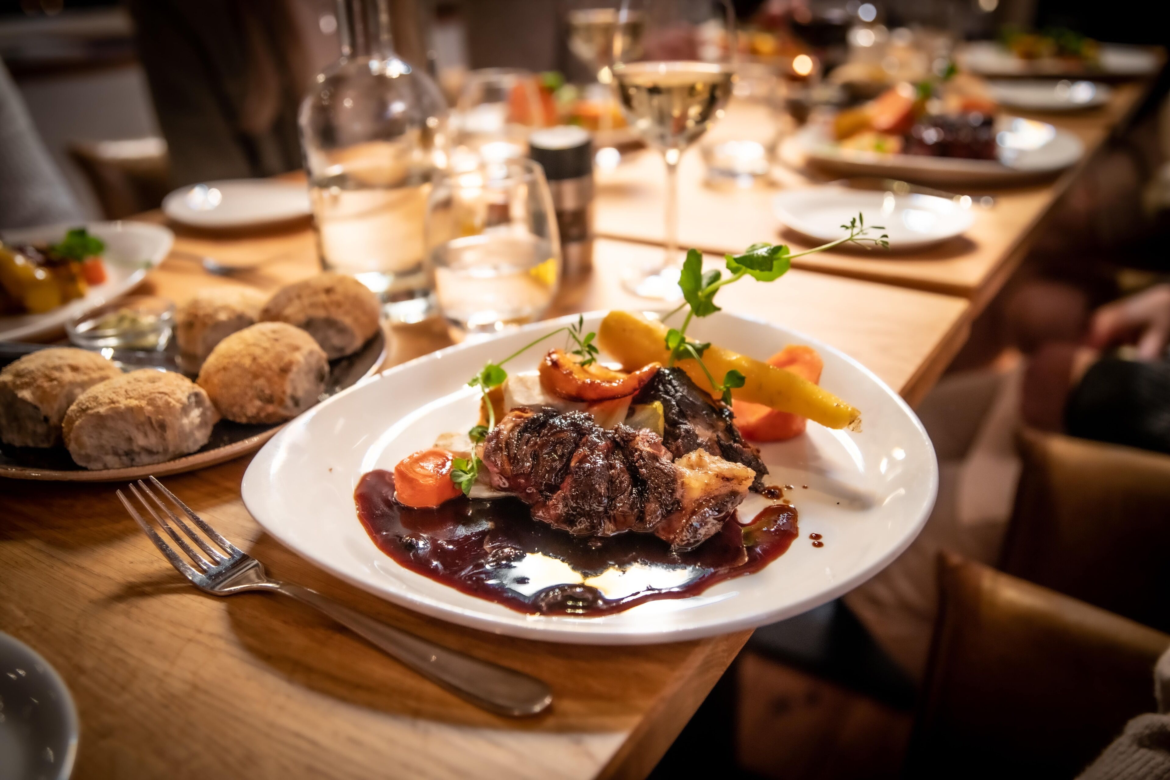 A dining table with a plate of food, a fork, and a glass of white wine.