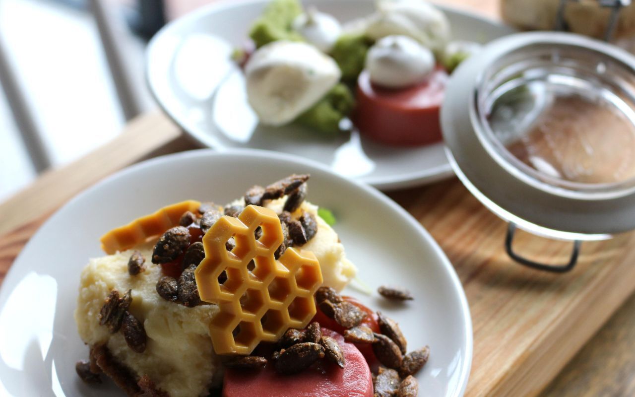 Une assiette avec un dessert surmonté d’une structure en forme de nid d’abeilles, de noix et d’une tranche de fruit rouge, peut-être une cerise.