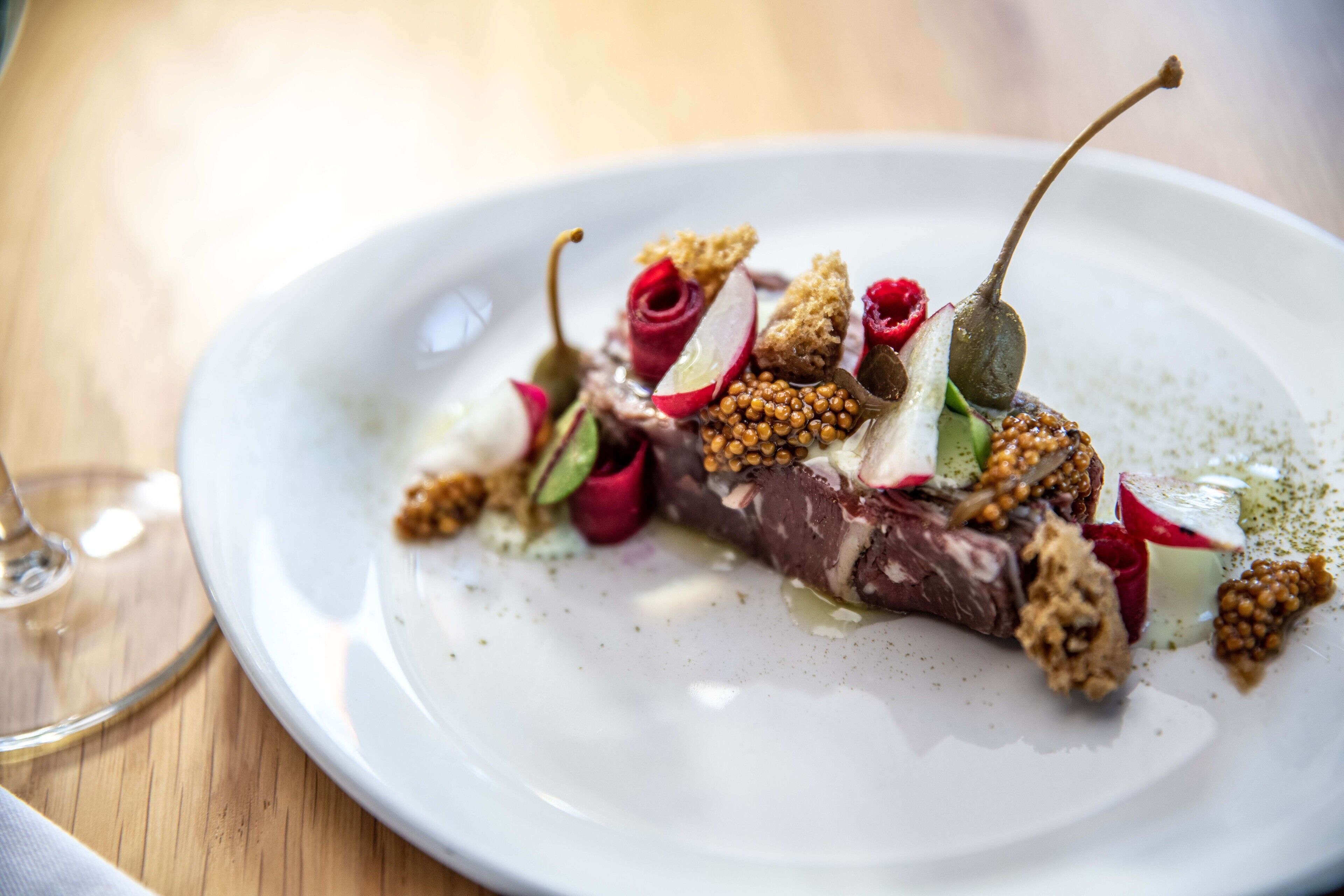 A white plate with a dish of food, a glass of wine, and a wooden table.