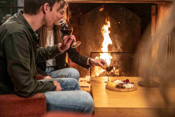 Una pareja sentada junto a la chimenea, con un plato de comida y copas de vino.