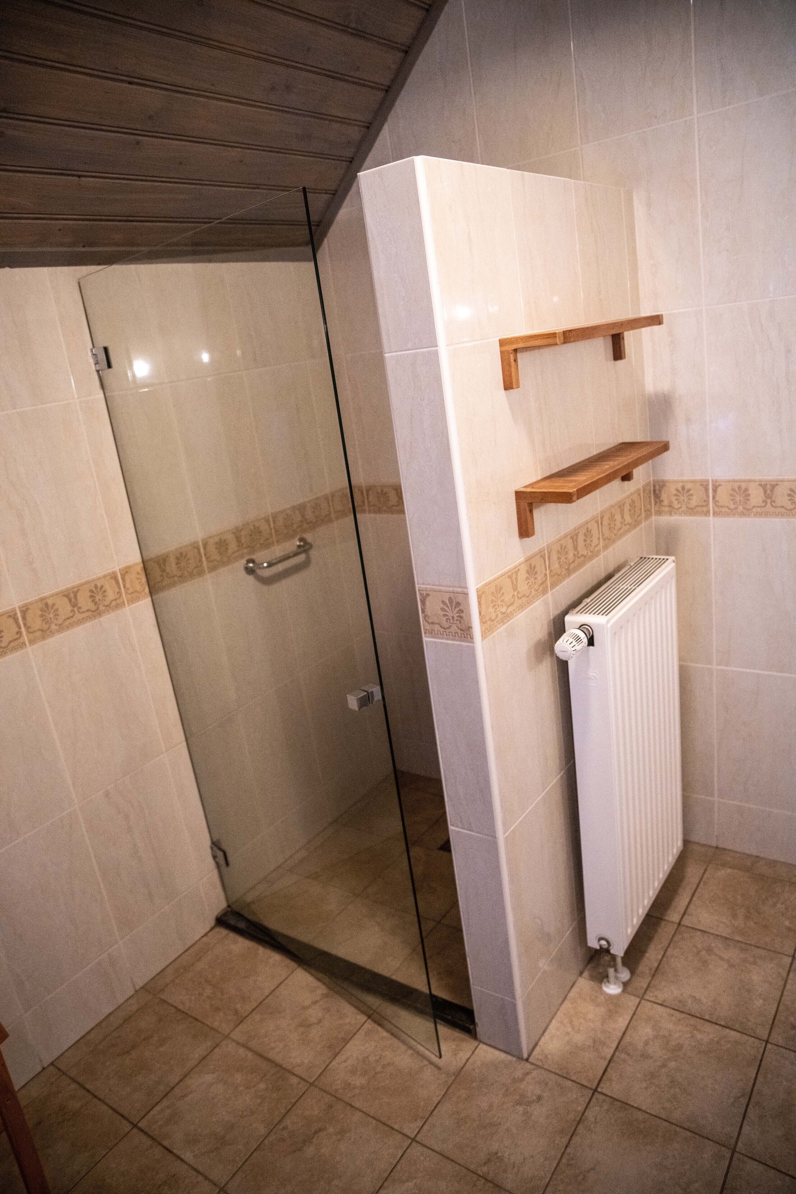 Un baño con cabina de ducha de vidrio, un radiador blanco y un estante de madera.