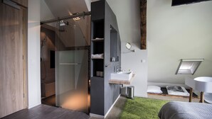 A modern bedroom with a built-in shower, a bedside table, a small window, and a green carpet. - Erfgoed Bossem (Lattrop)