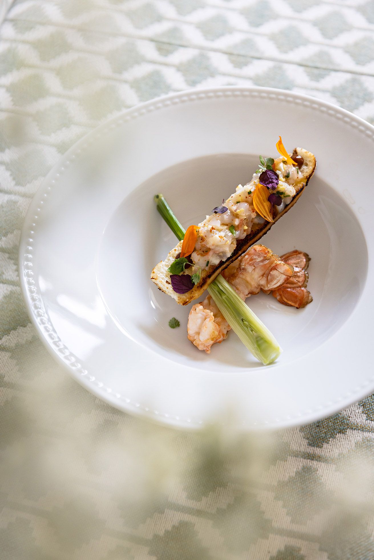 A white plate with a seafood dish, possibly crab, on a textured tablecloth.