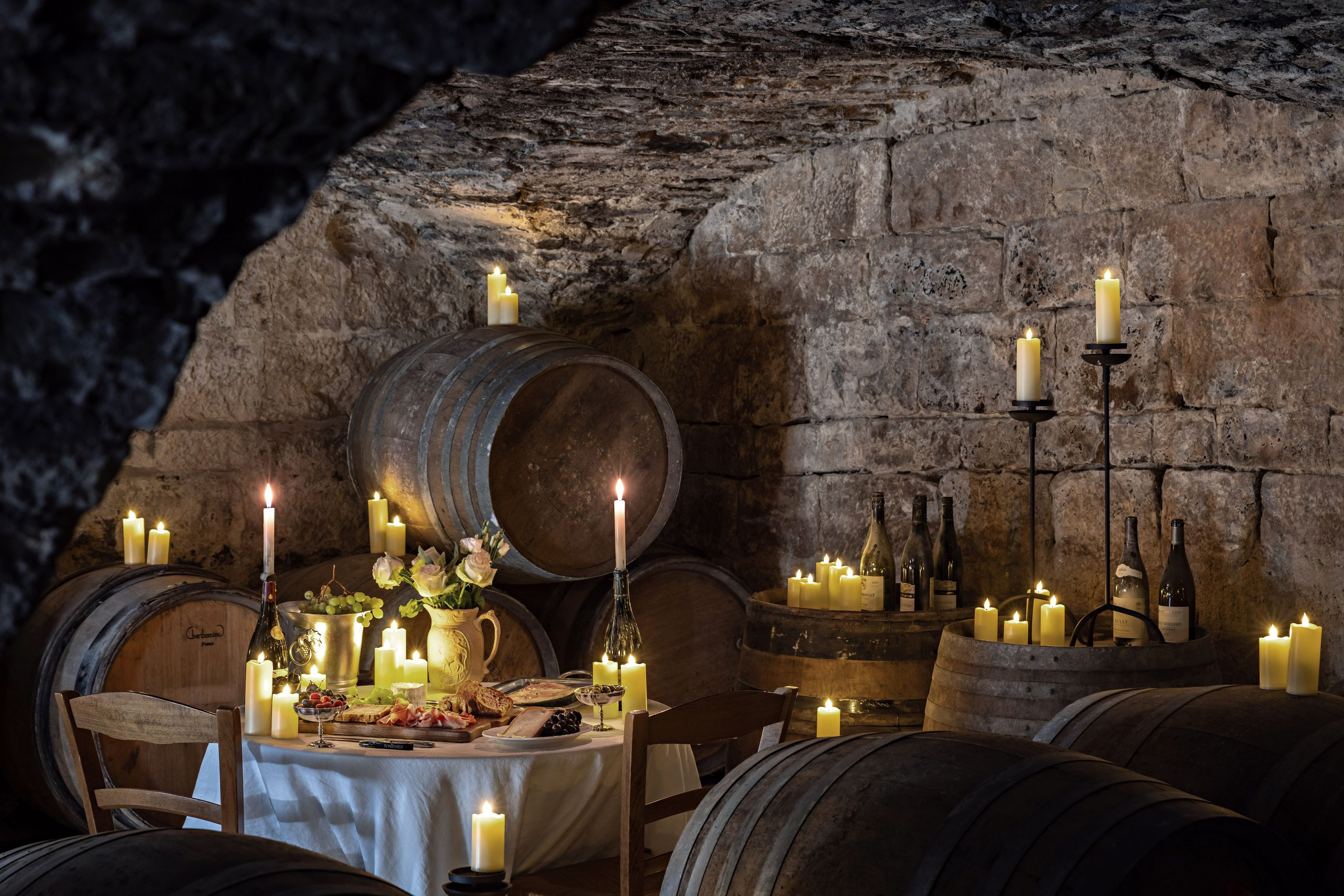 A rustic dining area with wooden barrels, candles, and wine bottles.