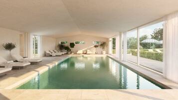 A modern indoor swimming pool with lounge chairs and large windows.