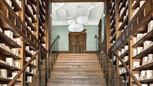 Eine Holztreppe mit Bücherregalen an beiden Seiten, die zu einem Raum mit einer Holztür und einem Deckenventilator führt.