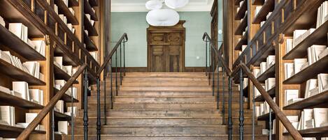 A wooden staircase with bookshelves on either side, leading to a room with a wooden door and a ceiling fan.