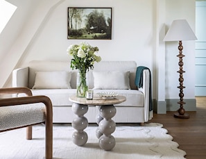 Een moderne woonkamer met een witte bank, een ronde tafel met een bloevas, en een hoge staande lamp.