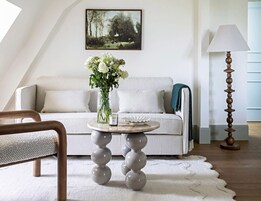 Una sala de estar moderna con un sofá blanco, una mesa redonda con un jarrón de flores y una lámpara de pie alta.