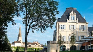 A large, historic building with a prominent tower in the background, surrounded by well-maintained gardens and outdoor seating areas.