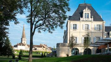 A large, historic building with a prominent tower in the background, surrounded by well-maintained gardens and outdoor seating areas.