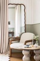 Una habitación con una mesa redonda de madera, una silla, un espejo y un jarrón con flores.