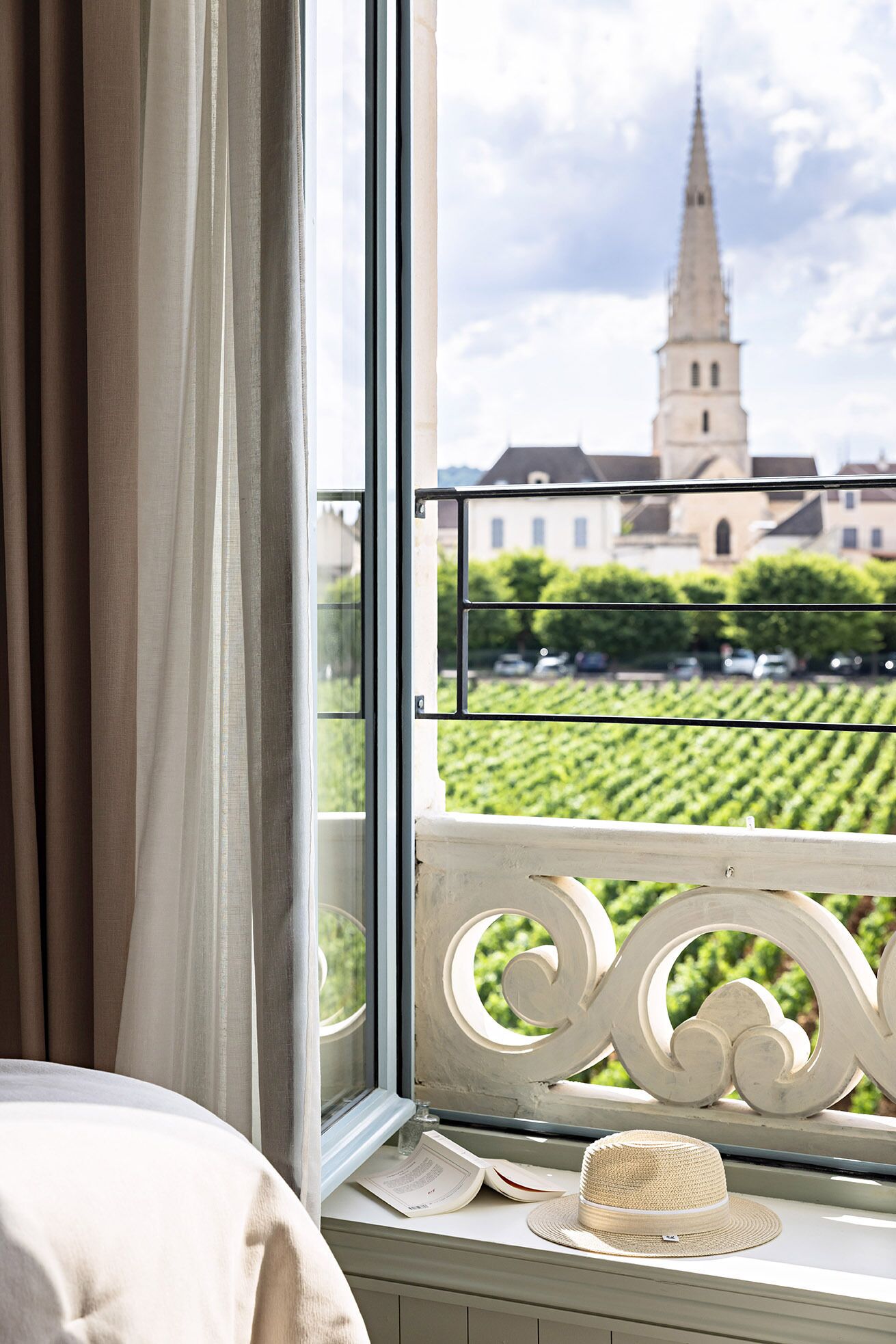 A window with a view of a church spire and a vineyard.
