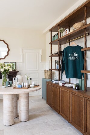 Una habitación ordenada con un mueble de madera que exhibe diversos objetos, una mesa con productos para el cuidado de la piel y una camisa verde sobre el mueble.