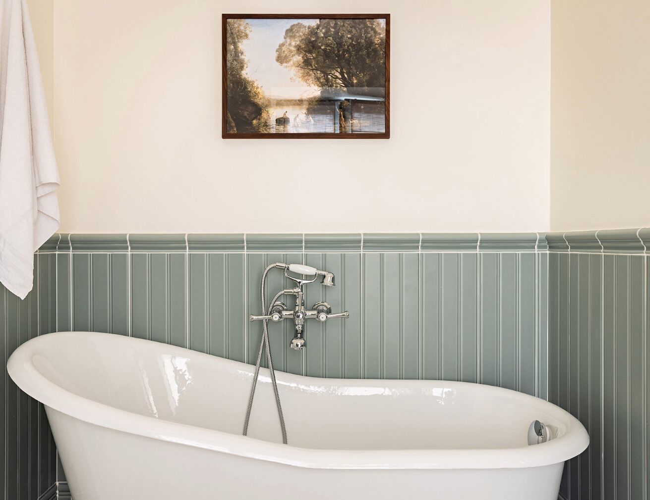 Une salle de bain avec une baignoire sur pieds, un tableau accroché au mur et une serviette suspendue au mur.